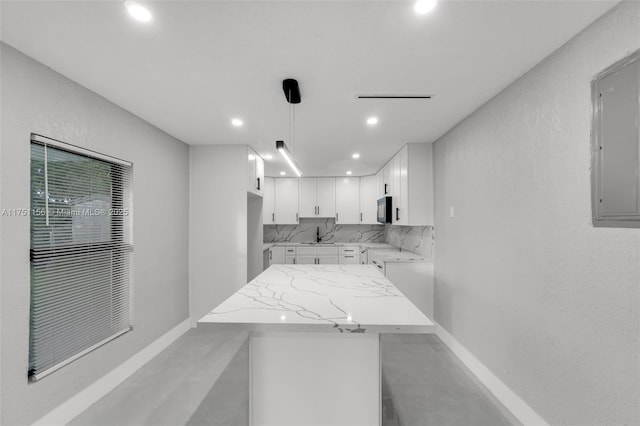 kitchen with black microwave, white cabinets, a center island, tasteful backsplash, and decorative light fixtures