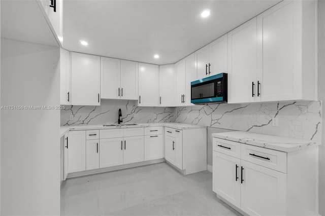 kitchen with backsplash, a sink, light stone countertops, and white cabinets