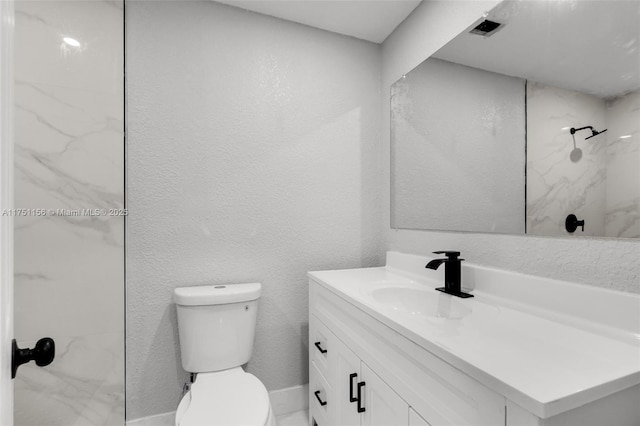 bathroom featuring toilet, a textured wall, a marble finish shower, and vanity