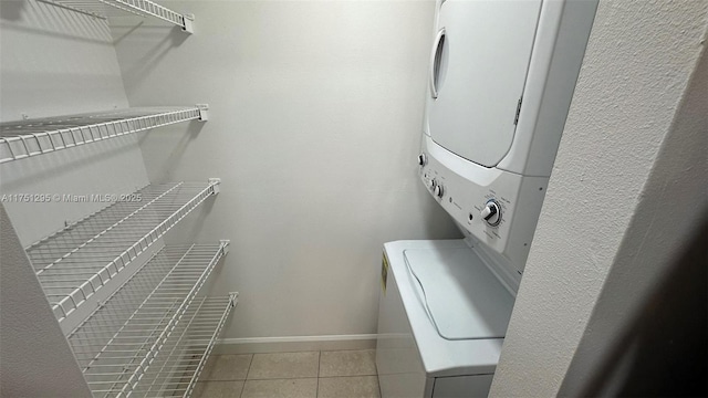 clothes washing area featuring light tile patterned floors, laundry area, stacked washing maching and dryer, and baseboards