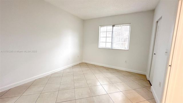 unfurnished bedroom with a textured ceiling, light tile patterned flooring, and baseboards