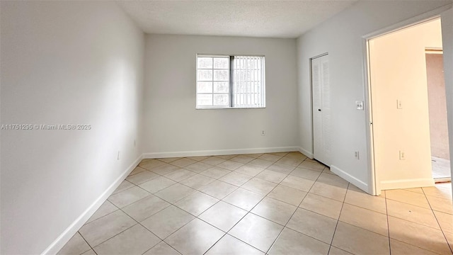 spare room featuring light tile patterned floors, baseboards, and a textured ceiling