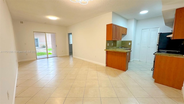 kitchen featuring light tile patterned floors, baseboards, light countertops, tasteful backsplash, and brown cabinetry