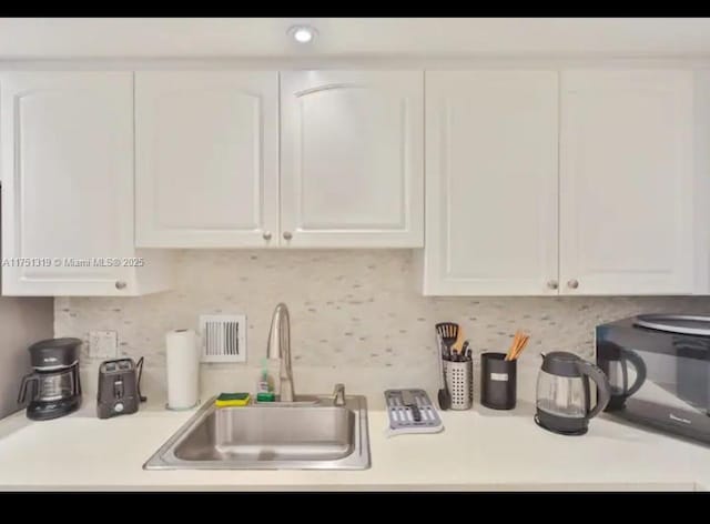 kitchen featuring decorative backsplash, white cabinets, light countertops, black microwave, and a sink