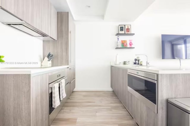 bar featuring wall oven, light wood-type flooring, a sink, and oven