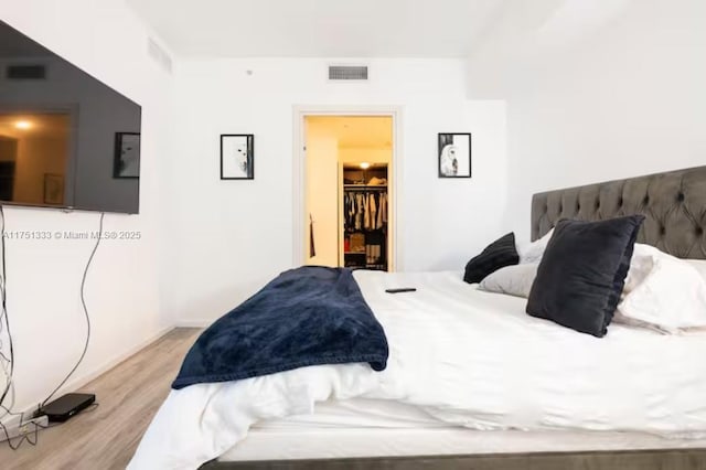 bedroom with light wood-type flooring, visible vents, and a spacious closet