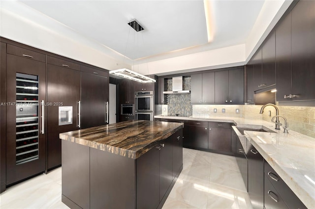 kitchen featuring a center island, backsplash, double oven, a sink, and wall chimney range hood