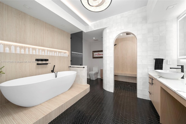 full bathroom with toilet, vanity, tile walls, a freestanding bath, and tile patterned floors