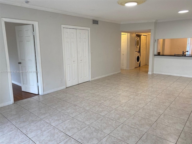 unfurnished bedroom featuring light tile patterned floors, baseboards, visible vents, stacked washer / dryer, and ornamental molding