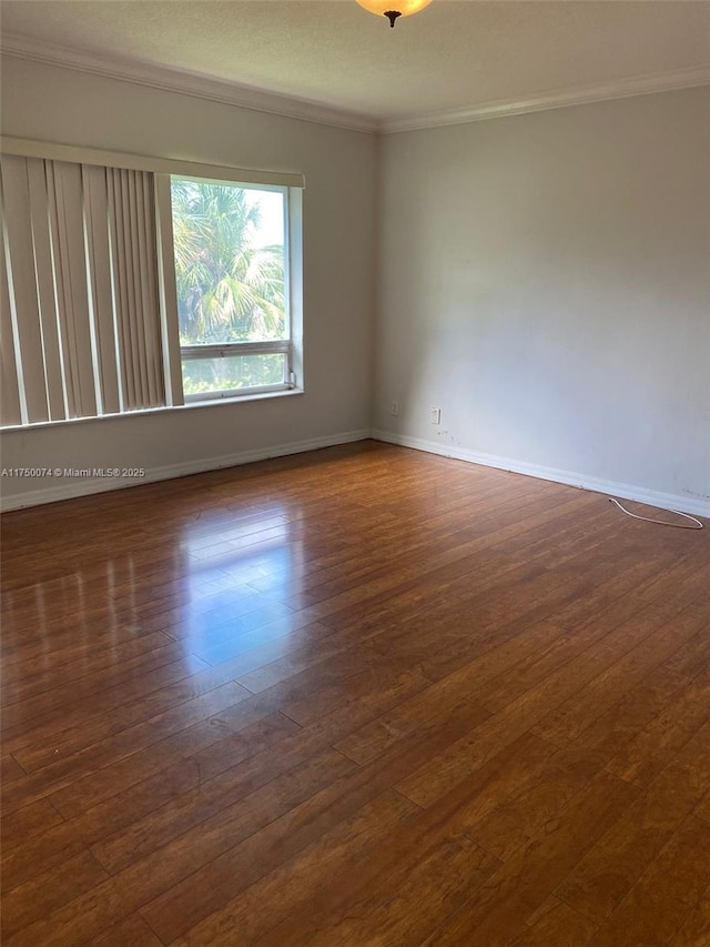 spare room with dark wood-type flooring, crown molding, and baseboards