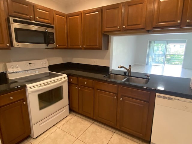 kitchen featuring dark countertops, white appliances, a sink, and light tile patterned floors