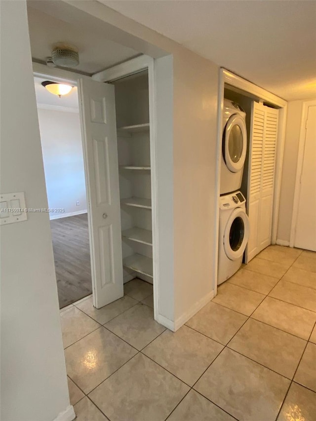 clothes washing area featuring stacked washer and clothes dryer, light tile patterned floors, baseboards, and laundry area