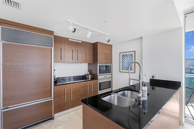 kitchen featuring visible vents, dark countertops, brown cabinets, built in appliances, and a sink