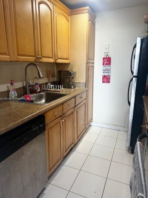 kitchen with a sink, light tile patterned flooring, stainless steel dishwasher, and freestanding refrigerator