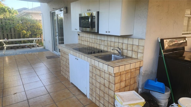 kitchen with tile countertops, stainless steel microwave, white cabinets, and a sink