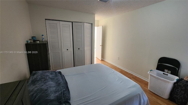 bedroom with a textured ceiling, light wood finished floors, a closet, and baseboards