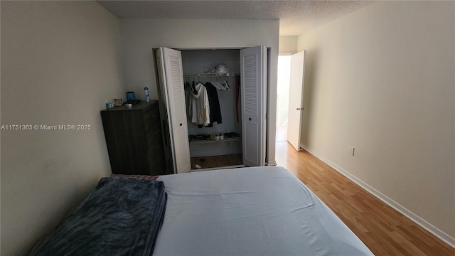 bedroom with a textured ceiling, a closet, baseboards, and wood finished floors