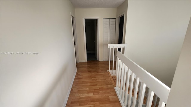 hall with a textured ceiling, light wood finished floors, an upstairs landing, and baseboards