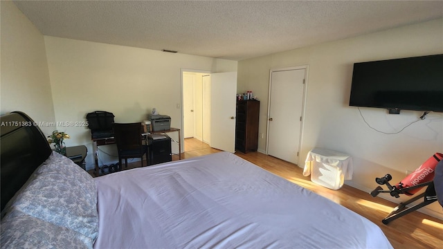 bedroom featuring light wood finished floors, visible vents, and a textured ceiling