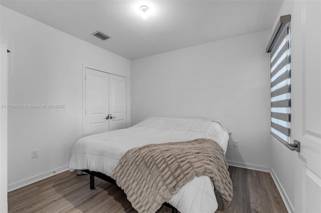 bedroom featuring baseboards, a closet, visible vents, and wood finished floors