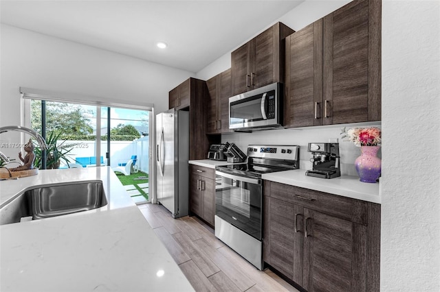 kitchen featuring a sink, light countertops, appliances with stainless steel finishes, dark brown cabinets, and wood tiled floor