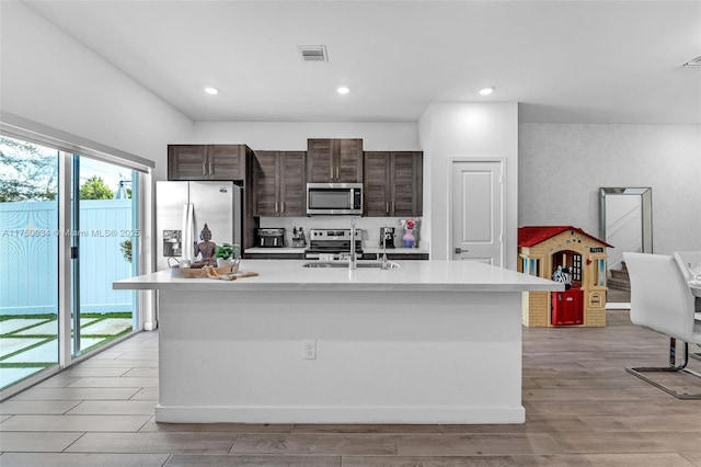 kitchen featuring stainless steel appliances, light countertops, a center island with sink, and dark brown cabinets