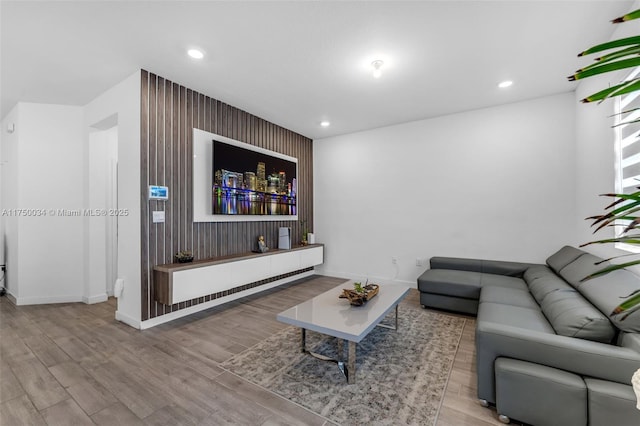 living room featuring light wood finished floors, an accent wall, baseboards, and recessed lighting