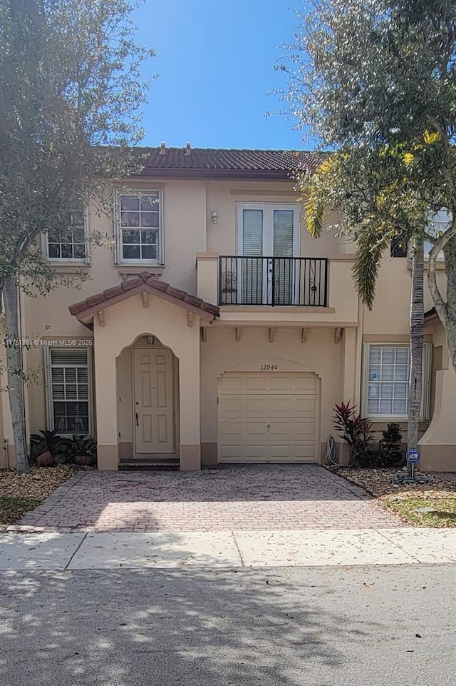 view of front of house with decorative driveway, an attached garage, a balcony, and stucco siding