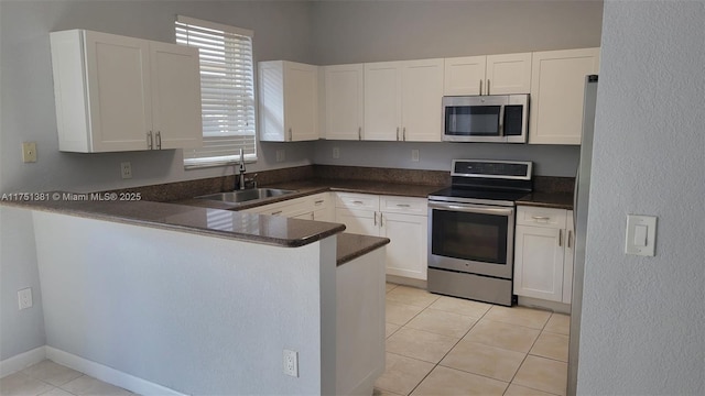 kitchen featuring stainless steel appliances, dark countertops, white cabinets, and a sink