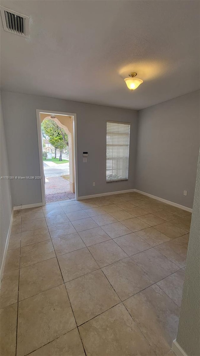 interior space with a textured ceiling, light tile patterned flooring, visible vents, and baseboards