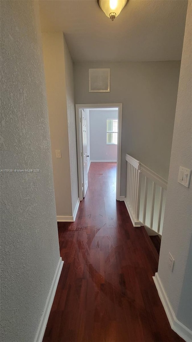 corridor featuring dark wood-style flooring, a textured wall, and baseboards