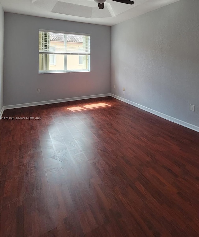 unfurnished room featuring dark wood-style floors, baseboards, a raised ceiling, and a ceiling fan