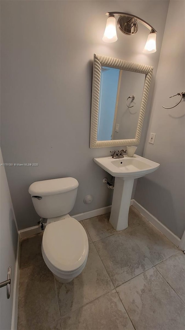 half bath with tile patterned flooring, toilet, and baseboards