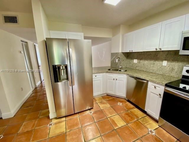 kitchen with visible vents, white cabinets, light stone countertops, stainless steel appliances, and a sink