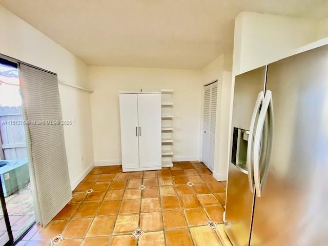 unfurnished bedroom with baseboards, stainless steel fridge with ice dispenser, and light tile patterned floors