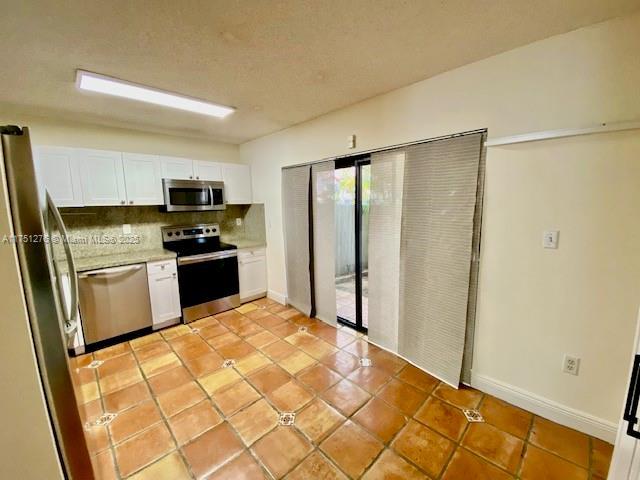 kitchen with light tile patterned floors, stainless steel appliances, tasteful backsplash, light countertops, and white cabinetry