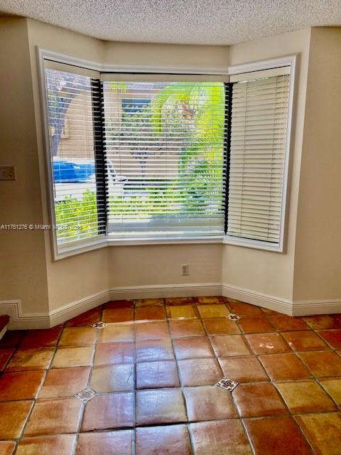 spare room with tile patterned flooring, baseboards, and a textured ceiling