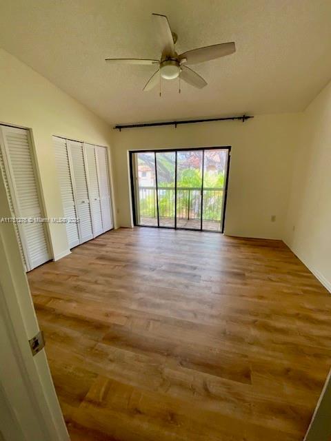 unfurnished bedroom featuring a ceiling fan, multiple closets, vaulted ceiling, access to exterior, and light wood finished floors