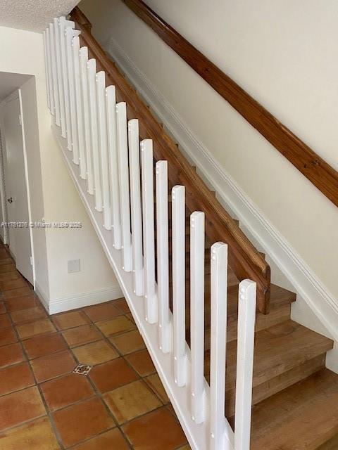 stairway featuring a textured ceiling, baseboards, and tile patterned floors