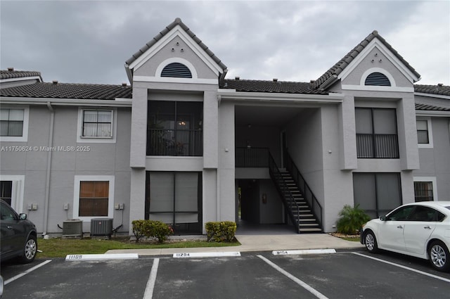 view of building exterior featuring central air condition unit, uncovered parking, and stairway