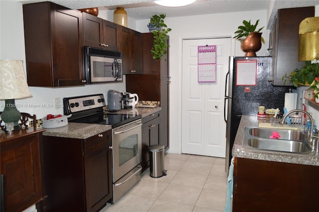 kitchen featuring light tile patterned floors, a textured ceiling, stainless steel appliances, a sink, and backsplash