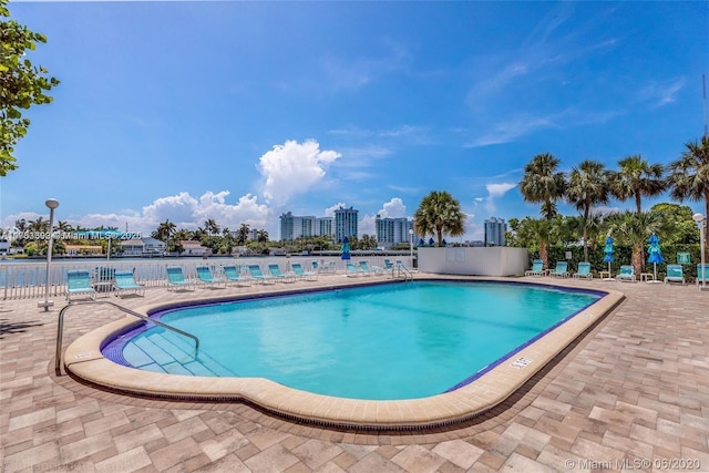 community pool with a patio area, fence, and a city view