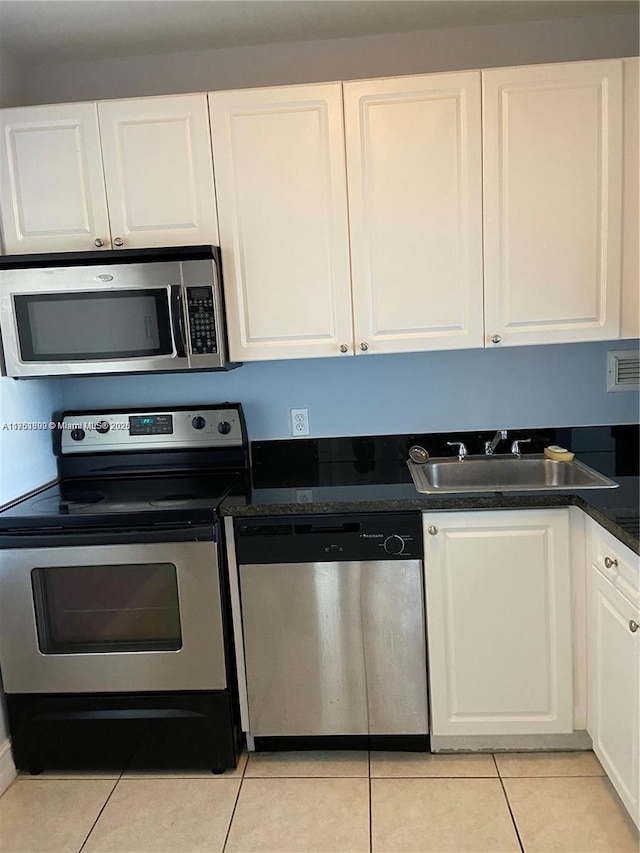 kitchen with light tile patterned floors, white cabinets, dark countertops, appliances with stainless steel finishes, and a sink