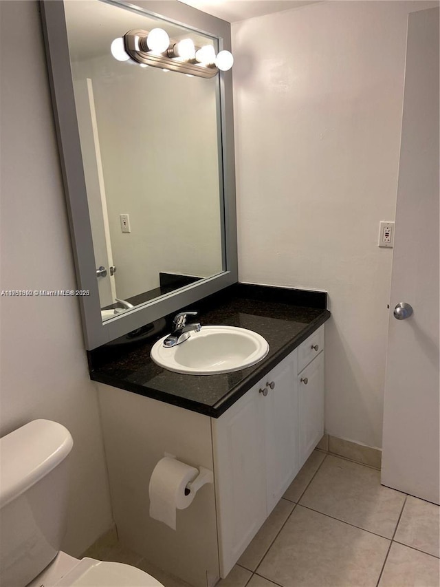 half bathroom featuring baseboards, vanity, toilet, and tile patterned floors