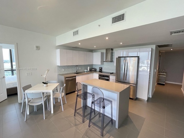 kitchen featuring visible vents, white cabinets, light countertops, appliances with stainless steel finishes, and wall chimney range hood