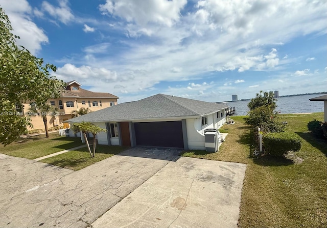 view of front of home with a shingled roof, concrete driveway, a water view, an attached garage, and a front yard