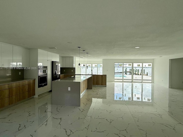 kitchen with pendant lighting, marble finish floor, white cabinetry, a kitchen island, and modern cabinets