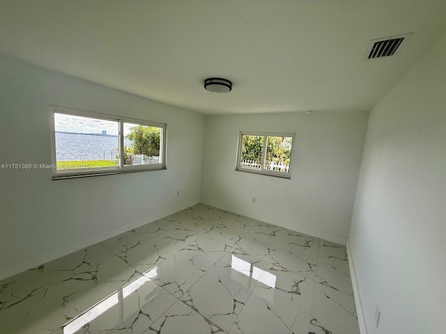 empty room featuring marble finish floor, a water view, visible vents, and a healthy amount of sunlight