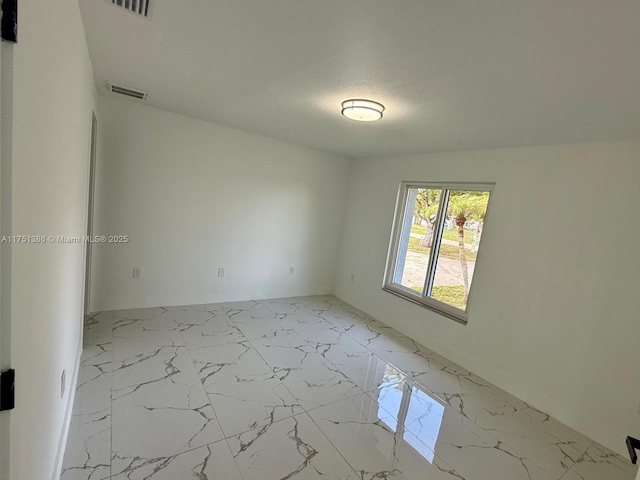 spare room featuring marble finish floor, visible vents, and a textured ceiling