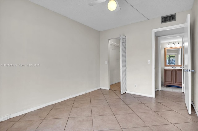 unfurnished bedroom featuring light tile patterned floors, visible vents, a ceiling fan, a textured ceiling, and baseboards